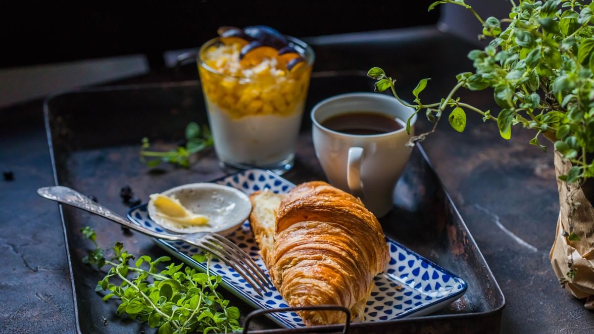 A delicious breakfast setup with a croissant, coffee, and yogurt parfait on a tray.